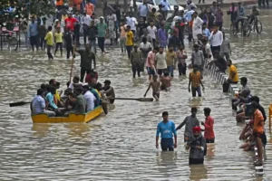 Crowds wade and paddle a makeshift boat through waist-deep monsoon floodwaters on a busy New Delhi street, July 2023.