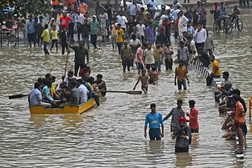 Crowds wade and paddle a makeshift boat through waist-deep monsoon floodwaters on a busy New Delhi street, July 2023.